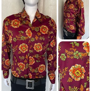 May include: A long-sleeved shirt with a burgundy background and a floral pattern in shades of orange, yellow, green, and brown. The shirt has a button-down collar and a long sleeve.
