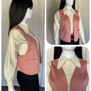 May include: A pink corduroy vest with two pockets and a button closure. The vest is worn over a white collared shirt.