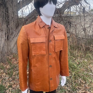 May include: A brown leather jacket with a button-up front and two large pockets on the chest.