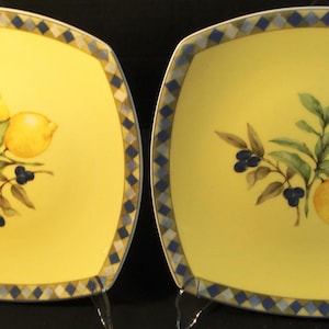 May include: Two square yellow plates with a lemon and olive branch design. The plates have a blue and white checkered border. The lemons are yellow, the olives are dark blue, and the leaves are green.