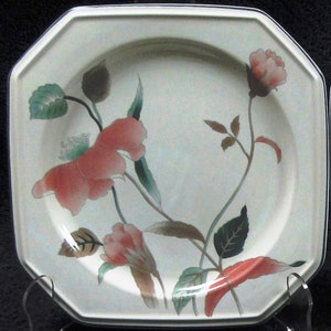 May include: Octagonal white plate with a floral design. The plate features pink and red flowers with green leaves and brown stems. The rim has a thin blue border. The plate is displayed on a clear stand.