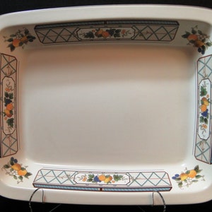 May include: A white ceramic baking dish with a blue and green floral design featuring fruit and vines. The dish has a rectangular shape with rounded corners.