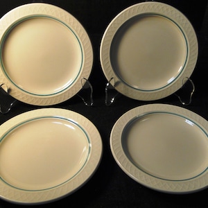 May include: A set of four round, off-white ceramic dinner plates. Each plate features a textured, embossed lattice pattern along the rim, accented by a thin, circular teal band that separates the rim from the smooth, flat center area.