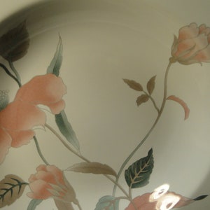 Pu&ograve; includere: Piatto in ceramica color crema con un motivo floreale. Il design presenta rose color pesca, foglie verdi e steli marroni. Il piatto ha un bordo leggermente curvo e una superficie liscia.