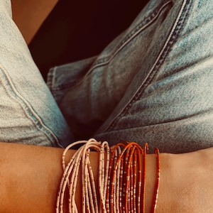 Pode incluir: Um conjunto de pulseiras de contas em tons de rosa e laranja. As pulseiras são feitas de contas pequenas e redondas e têm um brilho sutil.