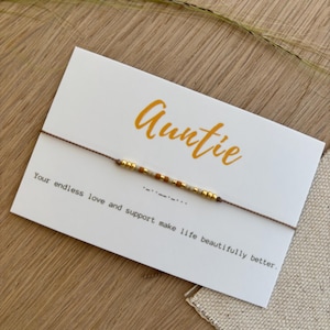 Könnte beinhalten: Auntie-Armband auf einer weißen Karte mit dem Text "Auntie" in orangefarbener Schrift. Das Armband hat goldene und braune Perlen. Die Karte trägt auch den Text "Your endless love and support make life beautifully better."
