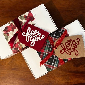 May include: Two white rectangular gift boxes. One box features a red rose floral pattern band with a dark red ribbon and a red tag with the white text for you. The other box has a green and red plaid band with a red ribbon and a tan tag with the red text for you.