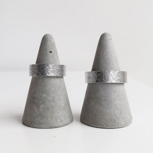 May include: Two silver hammered rings displayed on grey concrete cone-shaped ring holders.