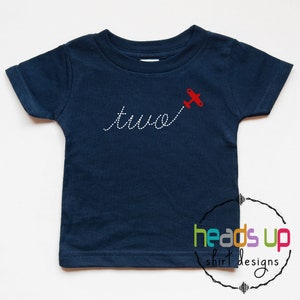 May include: A navy blue t-shirt with a red aeroplane flying over the word "two" in white stitching. The shirt is a toddler size and has a white tag on the collar.
