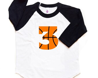 Può includere: Maglietta da baseball bianca e nera con maniche raglan e un numero 3 a forma di pallacanestro sul davanti.