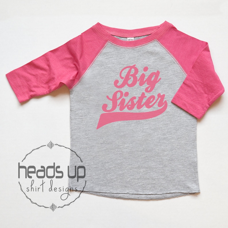 May include: A pink and grey long-sleeved shirt with a pink baseball-style graphic that says "Big Sister".