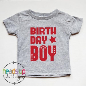 May include: A gray short-sleeved t-shirt with the words "BIRTHDAY BOY" in red letters with white stars.