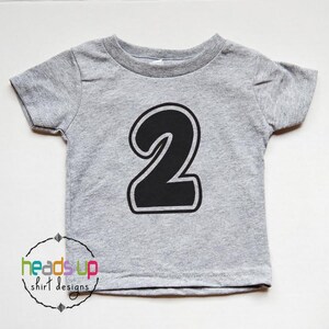 May include: A gray short-sleeved t-shirt with a black number "2" printed on the front. The number is outlined in white.