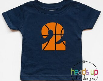 Può includere: Una maglietta blu navy a maniche corte con un grande numero "2" a forma di palla da basket arancione sul davanti. La palla da basket ha cuciture nere.