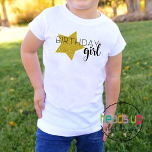 May include: White t-shirt with a gold glitter star and the text "Birthday girl".