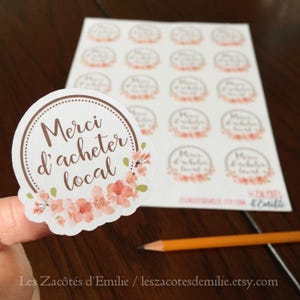 Sticker "Merci d'acheter local" with a wreath of flowers, on white paper