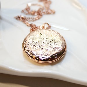 May include: A rose gold locket necklace with a delicate floral design. The locket is round and has a hinged lid.