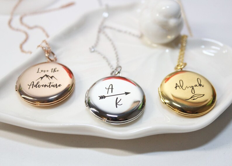 Puede incluir: Tres collares con medallones personalizados en oro rosa, plata y oro. El medall&oacute;n de oro rosa tiene el texto "Love the Adventure" con un gr&aacute;fico de monta&ntilde;a. El medall&oacute;n de plata tiene las iniciales "A K" con una flecha. El medall&oacute;n de oro tiene el nombre "Aliyah".