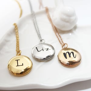 May include: Three gold, silver, and rose gold locket necklaces with engraved initials "L", "Liz", and "m".