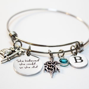 May include: Silver charm bracelet with a quote that reads "She believed she could... so she did". The bracelet also has charms of a medical symbol, a vial, a syringe, a teal blue crystal, and a letter B.