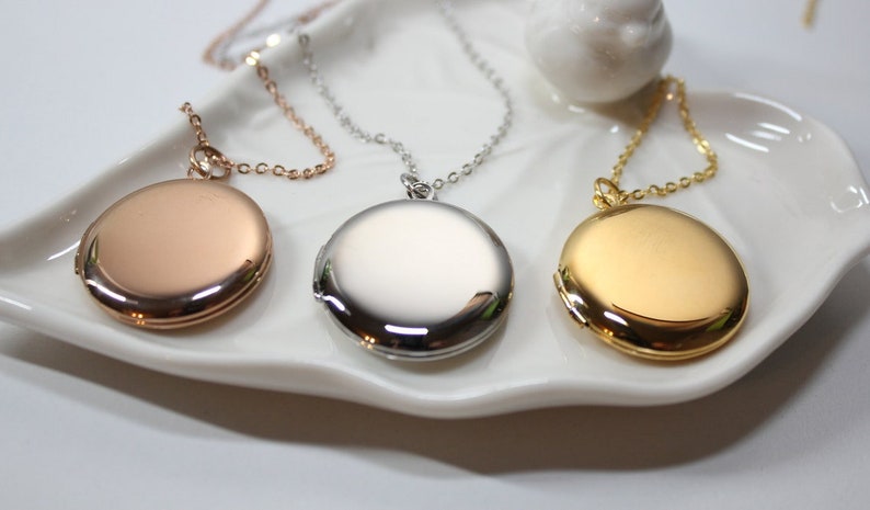 Puede incluir: Tres collares con medallones ovalados en oro rosa, plata y oro. Cada medall&oacute;n cuelga de una delicada cadena. Los medallones se exhiben en un plato blanco con forma de hoja.