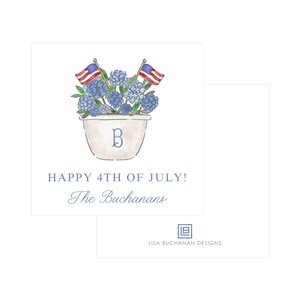 May include: A white planter with blue hydrangeas and two small American flags. The planter has a letter "B" painted on it. The text "HAPPY 4TH OF JULY! The Buchansans" is below the planter. The text "LISA BUCHANAN DESIGNS" is below the planter.