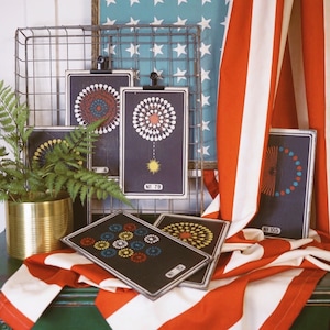 Peut inclure: Cinq cartes encadr&eacute;es noires avec des illustrations color&eacute;es de feux d'artifice. Les cartes sont num&eacute;rot&eacute;es et affich&eacute;es sur un rack en fil de fer avec un tissu ray&eacute; rouge, blanc et bleu en arri&egrave;re-plan.