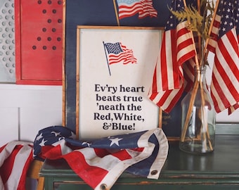 May include: A patriotic display featuring American flags, framed artwork, and decorative pieces in red, white, and blue. The artwork includes an American flag and the text "Ev'ry heart beats true 'neath the Red, White, & Blue!"