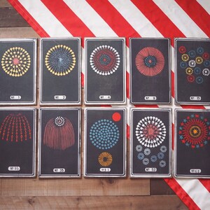 Peut inclure: Neuf cartes noires et blanches avec diff&eacute;rents motifs de feux d'artifice. Les cartes sont num&eacute;rot&eacute;es 1, 2, 4, 9, 15, 16, 35, 52 et 63.