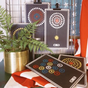 Peut inclure: Quatre cartes encadr&eacute;es noires avec des motifs de feux d'artifice color&eacute;s. Les cartes sont accroch&eacute;es &agrave; un rack en fil de fer avec un drapeau am&eacute;ricain rouge, blanc et bleu en arri&egrave;re-plan.