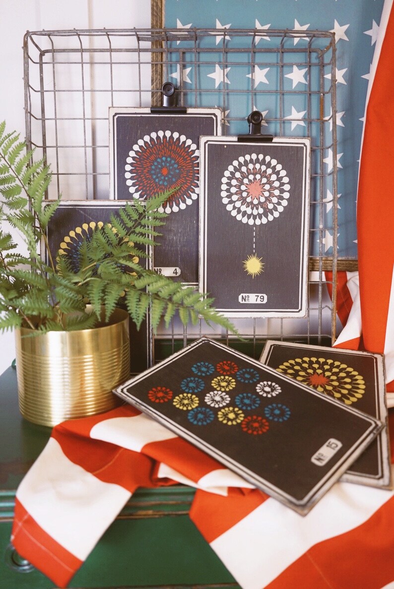 Peut inclure: Quatre cartes encadr&eacute;es noires avec des motifs de feux d'artifice color&eacute;s. Les cartes sont accroch&eacute;es &agrave; un rack en fil de fer avec un drapeau am&eacute;ricain rouge, blanc et bleu en arri&egrave;re-plan.