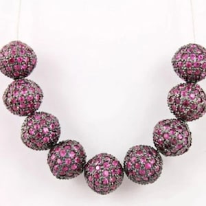 May include: A strand of pink gemstone beads with a silver finish. The beads are round and have a textured surface. The beads are strung on a clear thread.