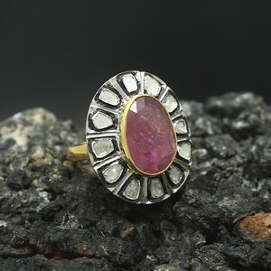 May include: A pink oval gemstone ring set in a silver and gold band. The ring is surrounded by a halo of smaller diamonds.