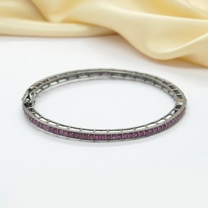 May include: A silver bangle bracelet with a row of small pink gemstones around the edge.