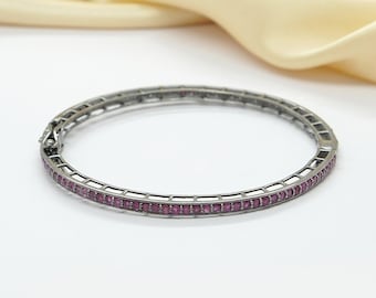 Puede incluir: Un brazalete de plata con una fila de pequeñas piedras preciosas rosas alrededor del borde.