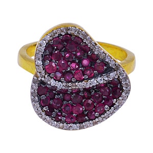 May include: A gold ring featuring a double-petal design, adorned with small red and white gemstones.