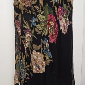 May include: Black dress with floral embroidery in shades of pink, blue, and gold. The dress features a high neckline and a layered design. The floral pattern is concentrated on the bodice and sleeves, with sequin accents.