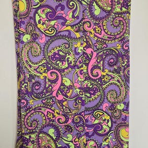 May include: Sleeveless dress with a vibrant paisley pattern in purple, pink, yellow, and green. The fabric features a repeating design of swirling floral and teardrop shapes, creating a bold, eye-catching look. The dress is hanging on a hanger.