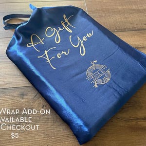 A blue satin gift bag with gold text and a logo, placed on a wooden surface.