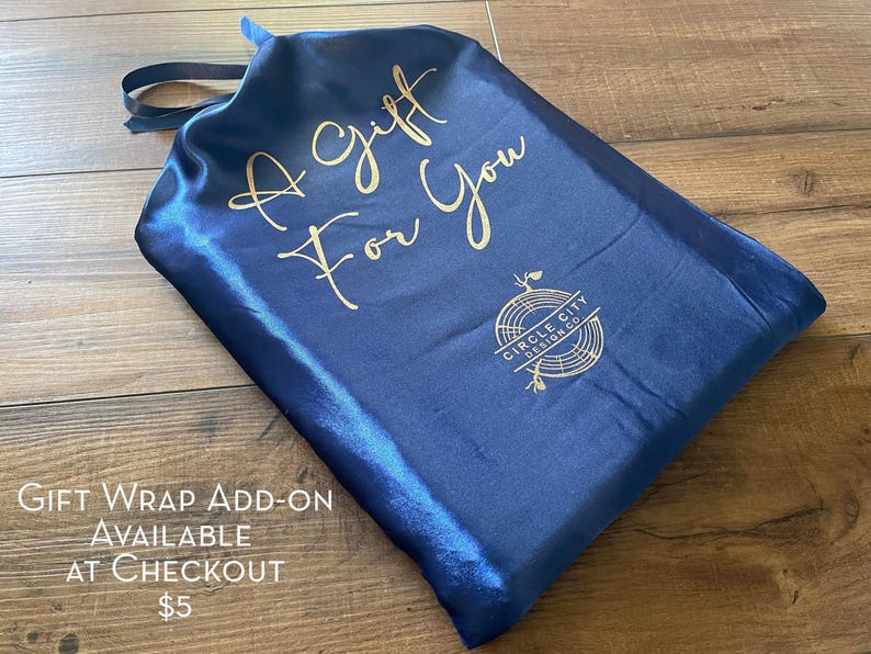 A blue satin gift bag with gold text and a logo, placed on a wooden surface.