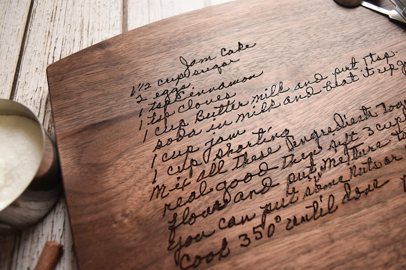 a wooden cutting board with handwritten text on it, along with some kitchen utensils and a bowl of sugar placed nearby.