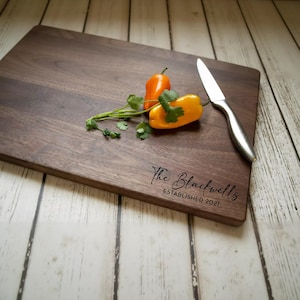 A wooden cutting board with a knife and two bell peppers on it, along with some parsley.