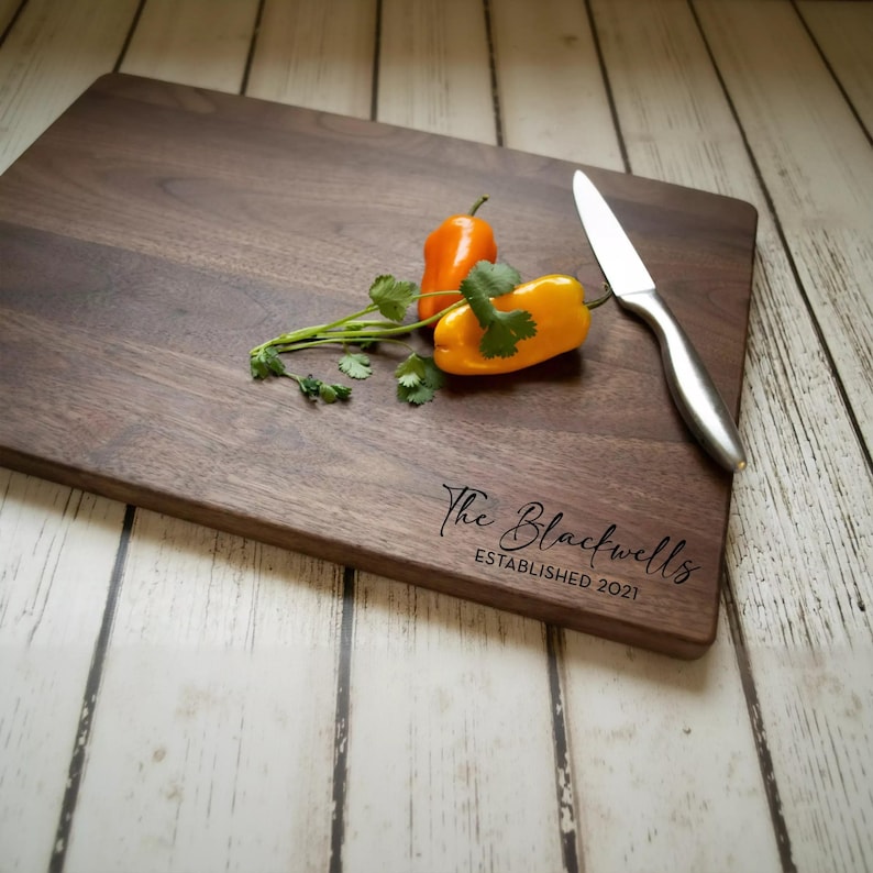A wooden cutting board with a knife and two bell peppers on it, along with some parsley.
