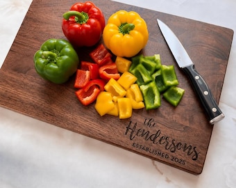 May include: A rectangular dark wood chopping board engraved with the text The Hendersons ESTABLISHED 2025. On the board are whole and chopped red, yellow, and green bell peppers alongside a silver paring knife with a black handle.