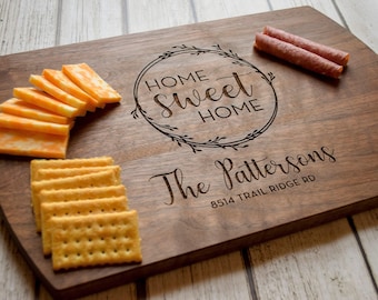 Puede incluir: Una tabla de servir de madera con las palabras "Home Sweet Home" y "The Pattersons" grabadas. Queso en rodajas, galletas saladas y dos trozos de salchicha están dispuestos en la tabla. La tabla mide 40 cm de largo.