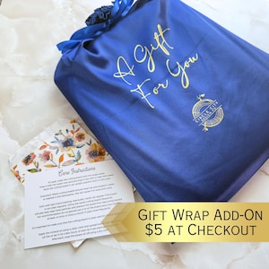 A blue satin gift bag with gold text and a logo, placed on a wooden surface.