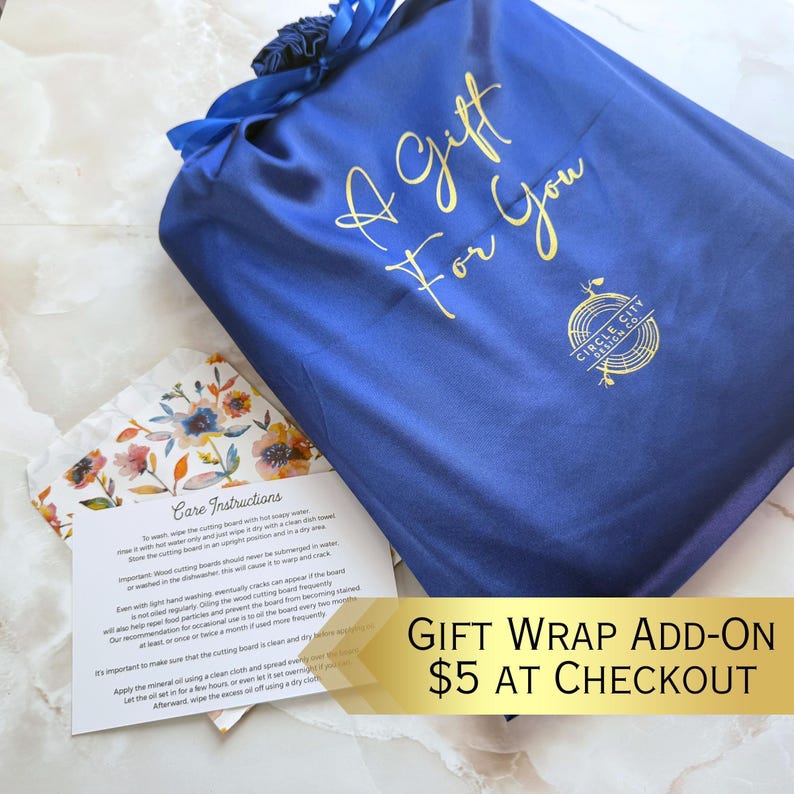 A blue satin gift bag with gold text and a logo, placed on a wooden surface.