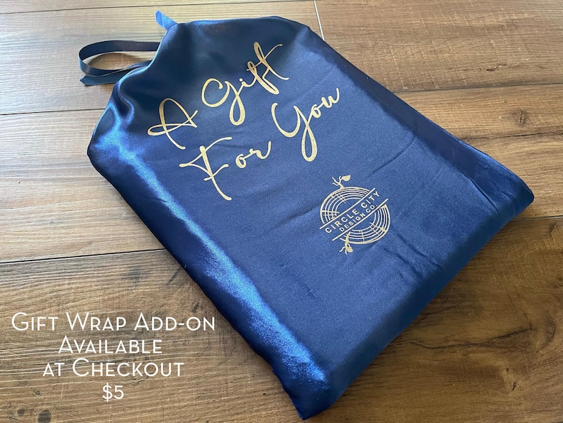 A blue satin gift bag with gold text and a logo, placed on a wooden surface.