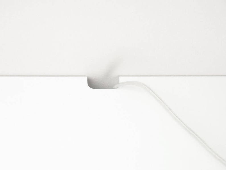 Puede incluir: Una superficie blanca con un corte para que pase un cable. Un cable blanco pasa a trav&eacute;s de la abertura.