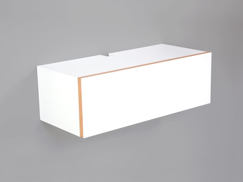 May include: White floating shelf with a wood trim around the edge. The shelf is mounted to a gray wall.